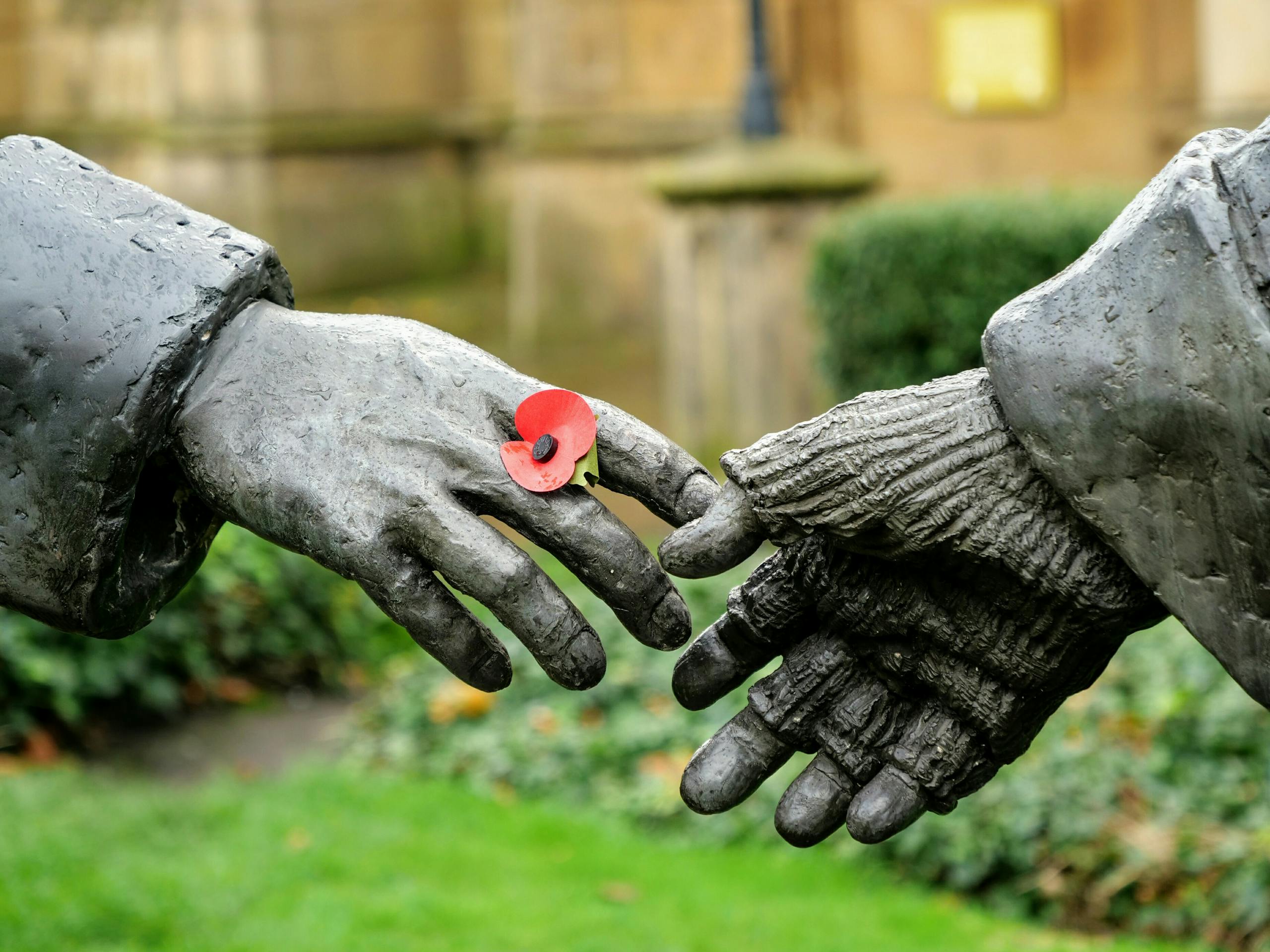 Close-up of statue hands holding a poppy flower symbolizing remembrance in Liverpool.